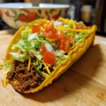 Close-up of an Air Fryer Tacos Extravaganza, filled with seasoned meat, lettuce, tomatoes, onions, and cheese.