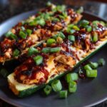 Two BBQ Chicken Zucchini Boats topped with green onions on a gray plate.