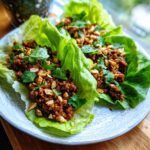 Two beef lettuce wraps on a plate, garnished with chopped peanuts and cilantro.