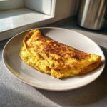 A golden cheesy omelette on a white plate, ready to eat. Perfect for a quick breakfast.