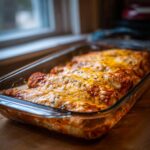A glass baking dish filled with Chicken Cottage Cheese Enchilada, topped with melted cheese and herbs.