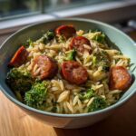 A bowl of Chicken Sausage Broccoli Orzo pasta dish, featuring sliced sausage and fresh broccoli florets.