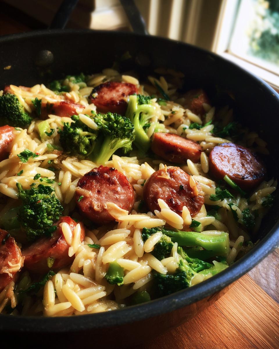 Close-up of Chicken Sausage Broccoli Orzo in a pan, featuring browned sausage slices and vibrant green broccoli.