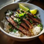 Close-up of a Cilantro Lime Steak Bowl with rice, sliced steak, cilantro, and lime wedges.