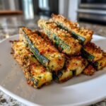 A stack of Crispy Baked Parmesan Zucchini sticks on a white plate, showing the golden-brown crust.