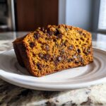 A slice of decadent pumpkin bread with chocolate chips on a white plate, showcasing its moist texture.