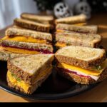 A platter of DIY Coffin Sandwiches Halloween, featuring turkey, cheese, and cranberry sauce on toasted bread.