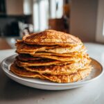 A stack of golden brown Energizing Red Lentil Pancakes on a white plate, ready to eat.