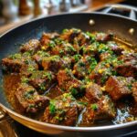 Close-up of Garlic Butter Beef Bites in a skillet, garnished with fresh herbs and garlic.