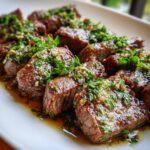 Close-up of juicy Garlic Butter Beef pieces topped with fresh herbs on a white plate.
