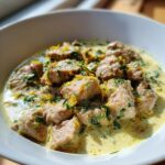A bowl of Ginger Lime Pork with Coconut, garnished with herbs and lime zest in a creamy sauce.