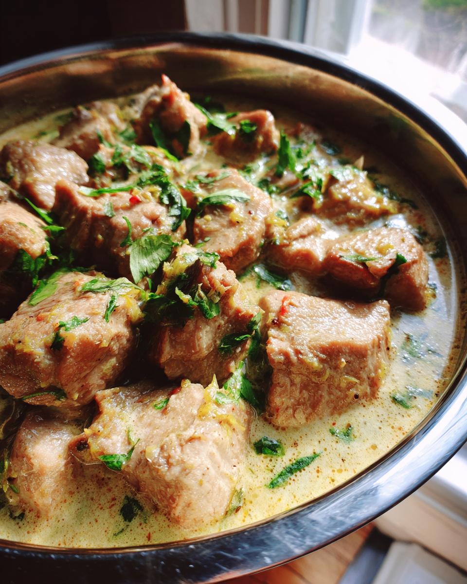 Close-up of Ginger Lime Pork with Coconut in a metal bowl, garnished with fresh herbs.