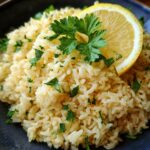 A bowl of Greek Lemon Rice garnished with fresh parsley and a lemon slice.