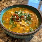 A bowl of Green Enchilada Chicken Soup topped with diced tomatoes, onions, and cilantro.