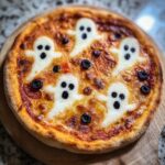 Overhead view of a Halloween pizza margherita with ghost-shaped mozzarella and black olive decorations.