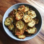 Overhead shot of a bowl filled with golden, crispy Healthy Zucchini Chips, seasoned with herbs and spices.
