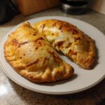 Two golden-brown High Protein Pizza Pockets on a white plate, one cut open to show the filling.