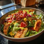 A vibrant bowl of High Protein Southwest Chicken Salad with chicken, lettuce, tomatoes, corn, red onion, and bacon.
