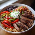 A vibrant High Protein Steak Fajita Bowl with steak, rice, peppers, beans, salsa, and sour cream.