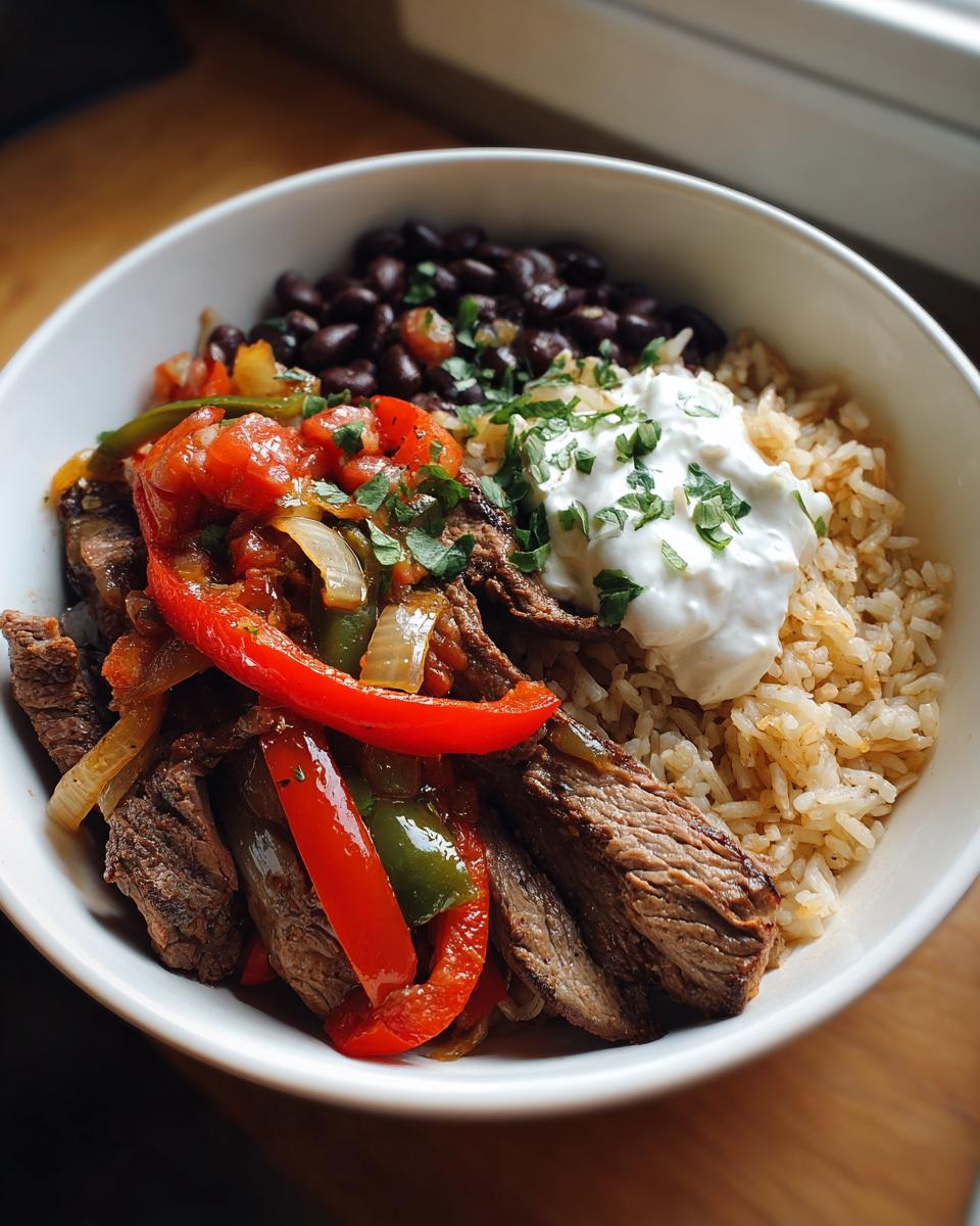 Overhead view of a High Protein Steak Fajita Bowl with rice, black beans, steak, peppers, onions, and sour cream.
