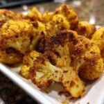 Close-up of Honey Curry Roasted Cauliflower florets on a white plate, showing the golden-brown color and texture.