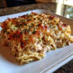 A slice of Ina Garten's Chicken Casserole Recipe, featuring pasta, chicken, and a golden, cheesy topping, garnished with parsley.