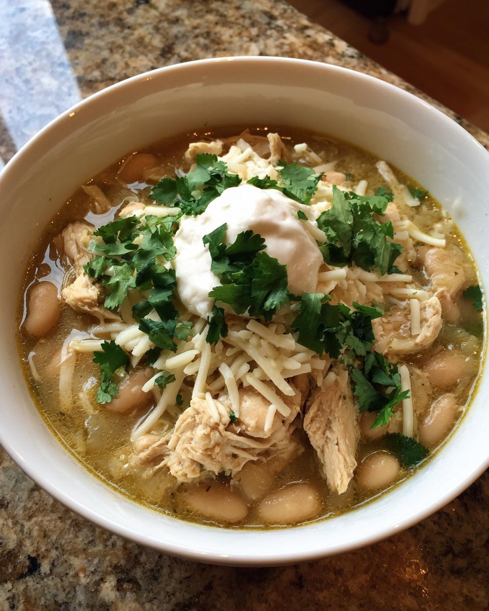 A bowl of killer white chili topped with shredded cheese, sour cream, and fresh cilantro.