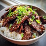 A delicious bowl of Korean BBQ Steak Rice topped with sliced green onions and sesame seeds.