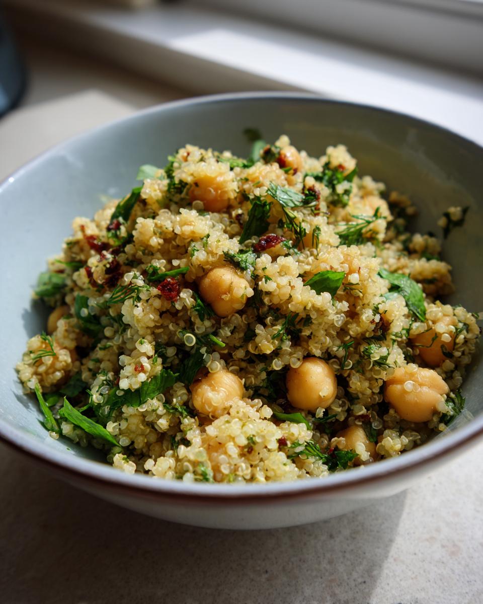 A bowl of Lemon Herb Quinoa Chickpeas salad, garnished with fresh herbs and sun-dried tomatoes.