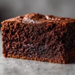 Detailed close-up of a rich, moist slice of low carb chocolate cake on a gray surface.
