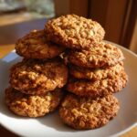 A stack of freshly baked Low Sugar Oatmeal Cookies on a white plate, showcasing their texture and golden-brown color.