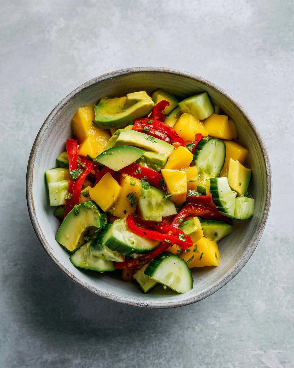 Overhead view of a colorful Mango Cucumber Salad with Avocado, red bell peppers, and herbs in a rustic bowl.