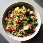 Overhead shot of a vibrant Mediterranean Quinoa Salad in a white bowl, featuring quinoa, cucumbers, olives, and red bell peppers.