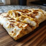 Two melty garlic chicken wraps stacked on a wooden board, showcasing the chicken and cheese filling.