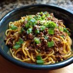 A bowl of Mongolian Ground Beef Noodles, topped with green onions and sesame seeds.