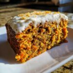 A single slice of No Sugar Carrot Cake with white frosting on a white plate.