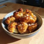 A bowl filled with golden brown Parmesan Cauliflower Bites, sprinkled with parmesan and herbs.