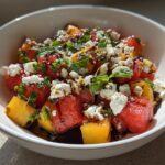 A bowl of Peach Watermelon Salad with feta cheese, mint, and balsamic glaze.