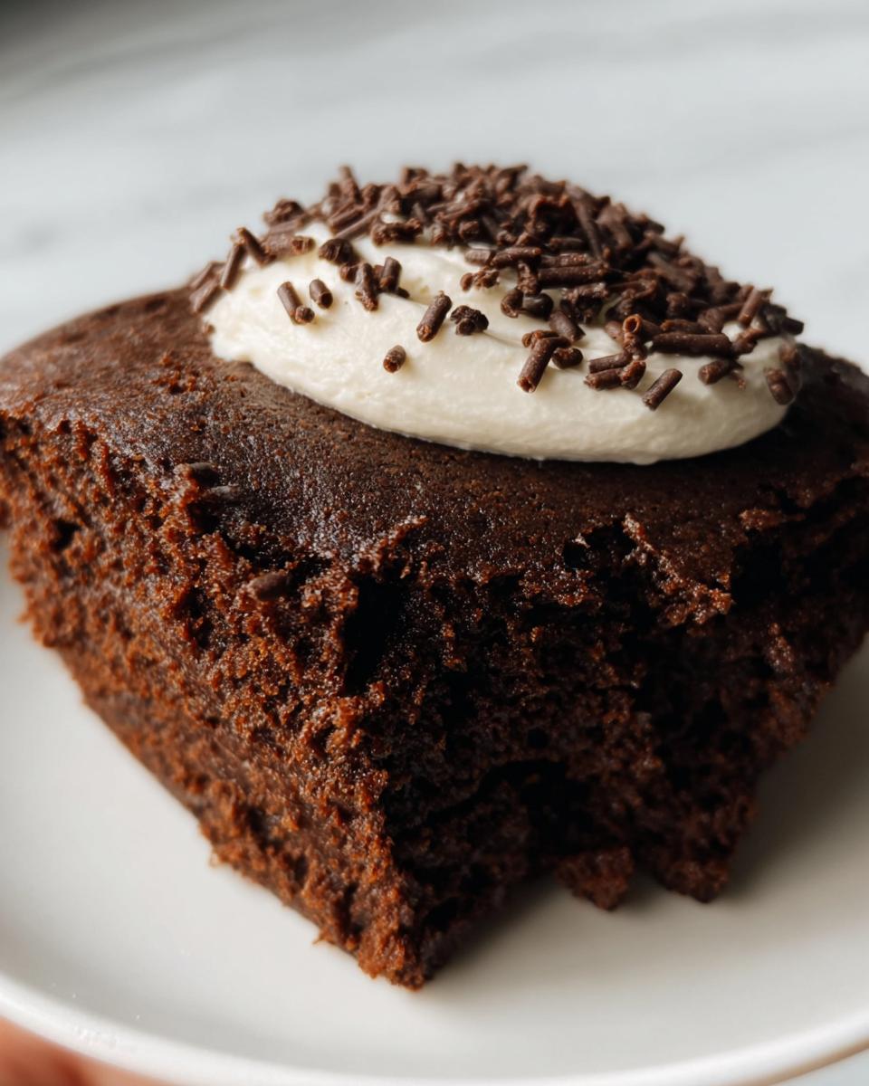 A single Protein Brownie topped with white cream and chocolate sprinkles on a white plate.