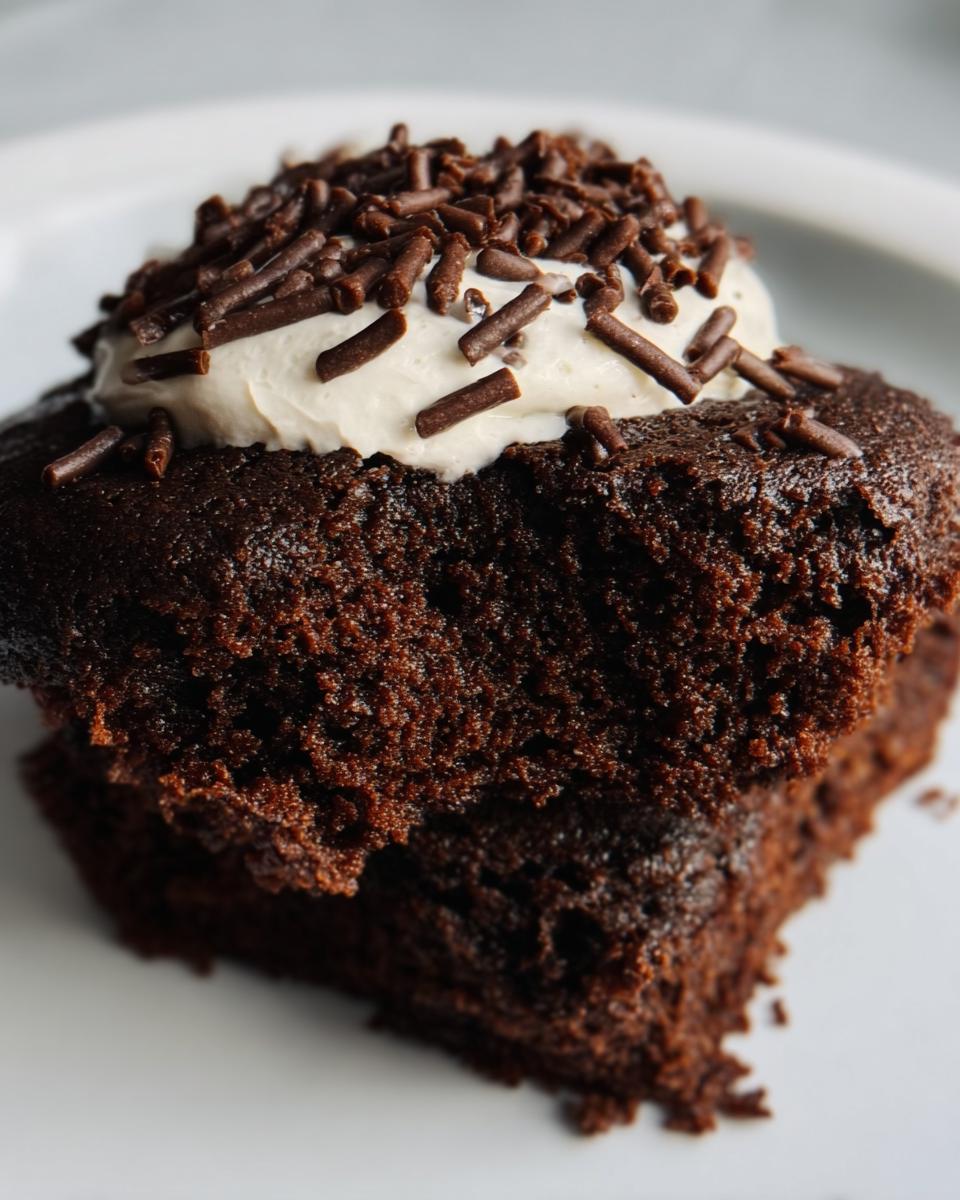 Close-up of a moist Protein Brownie topped with cream and chocolate sprinkles on a white plate.