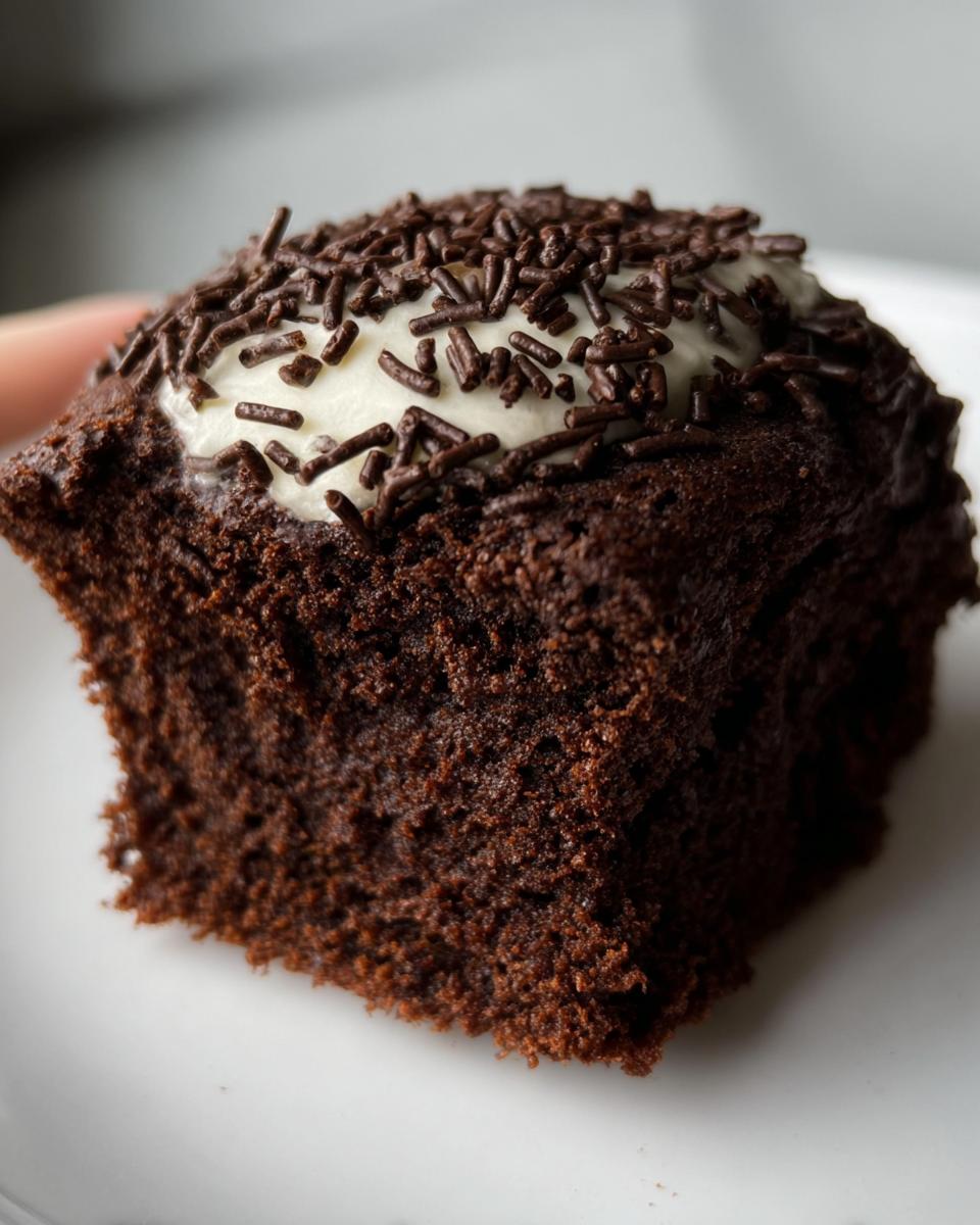 Close-up of a Protein Brownie topped with white frosting and chocolate sprinkles on a white plate.