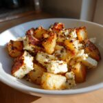 Close-up of a bowl filled with crispy Roasted Potatoes with Baked Feta and herbs.