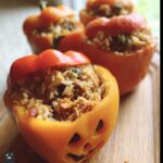 Orange bell pepper carved with a jack-o'-lantern face, filled with shredded chicken and rice for SHREDDED CHICKEN RICE STUFFED PEPPERS HALLOWEEN.