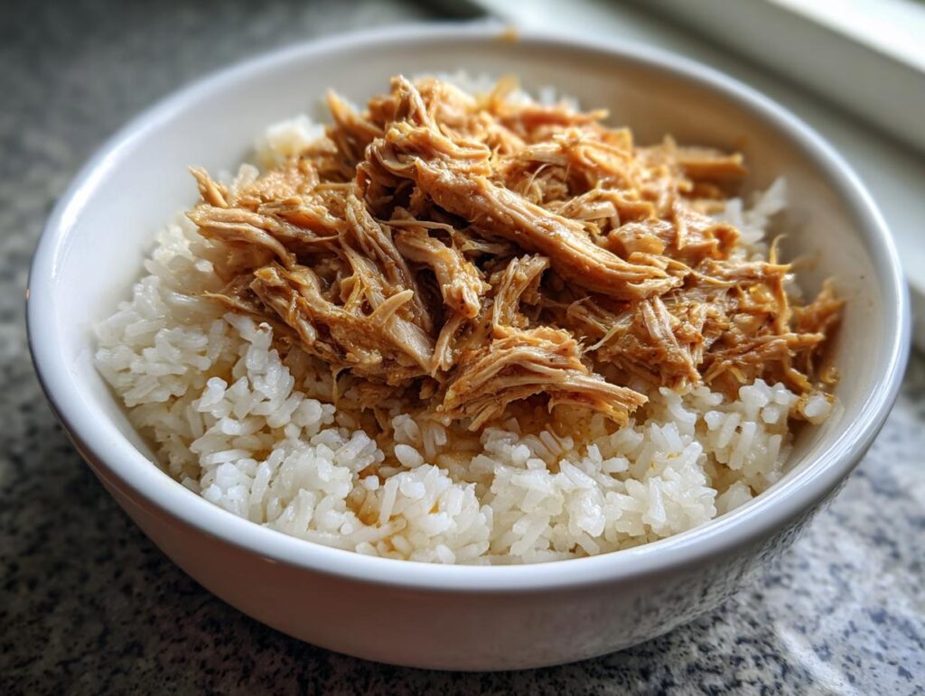 A white bowl filled with fluffy white rice topped with shredded Slow Cooker Chicken and Rice.