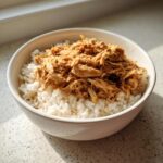 A bowl of delicious Slow Cooker Chicken and Rice, with shredded chicken on top of fluffy white rice.