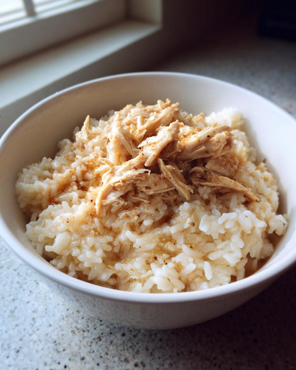 A white bowl filled with creamy slow cooker chicken and rice, seasoned and ready to eat.