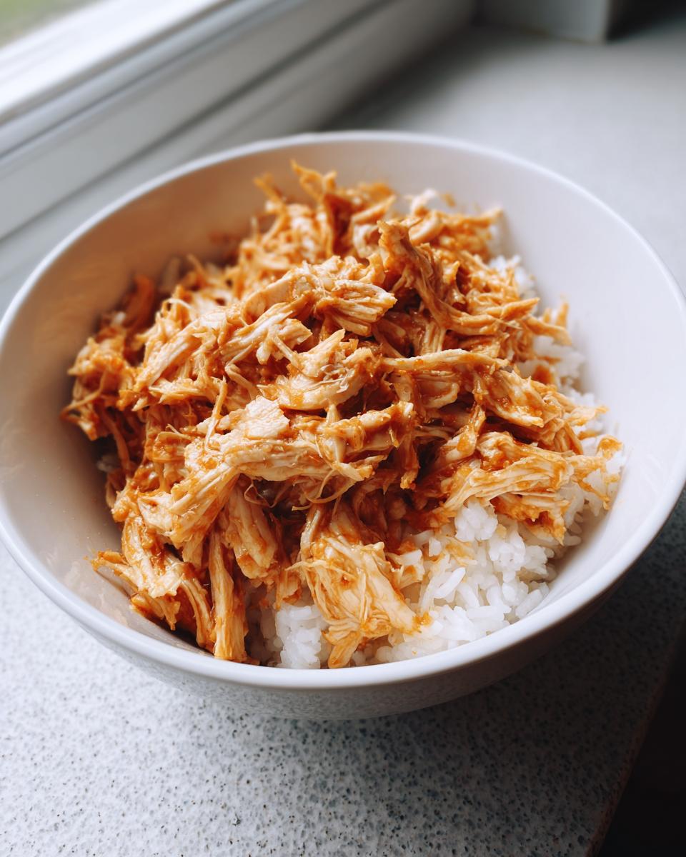 A bowl of Slow Cooker Chicken and Rice, featuring shredded chicken over a bed of fluffy white rice.