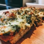 Close-up of a slice of Spinach Pesto Butter Bean bake on a wooden board, showcasing the pesto topping and cheesy layer.