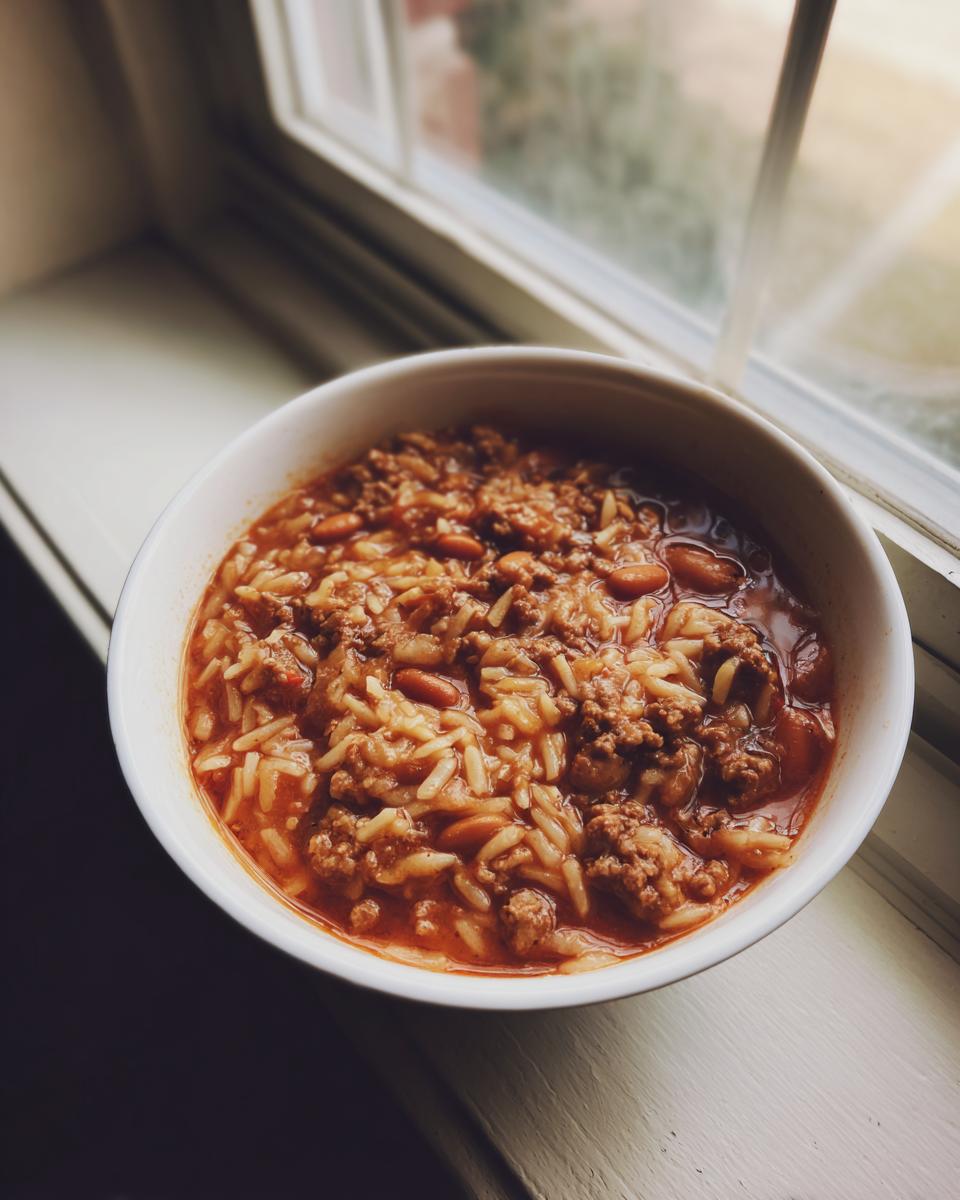 A bowl of Taco Rice Soup with ground beef, rice, and beans, sitting on a windowsill.