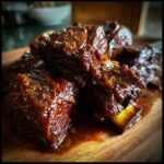 Close-up of tender braised short ribs with a rich sauce, served on a wooden board.